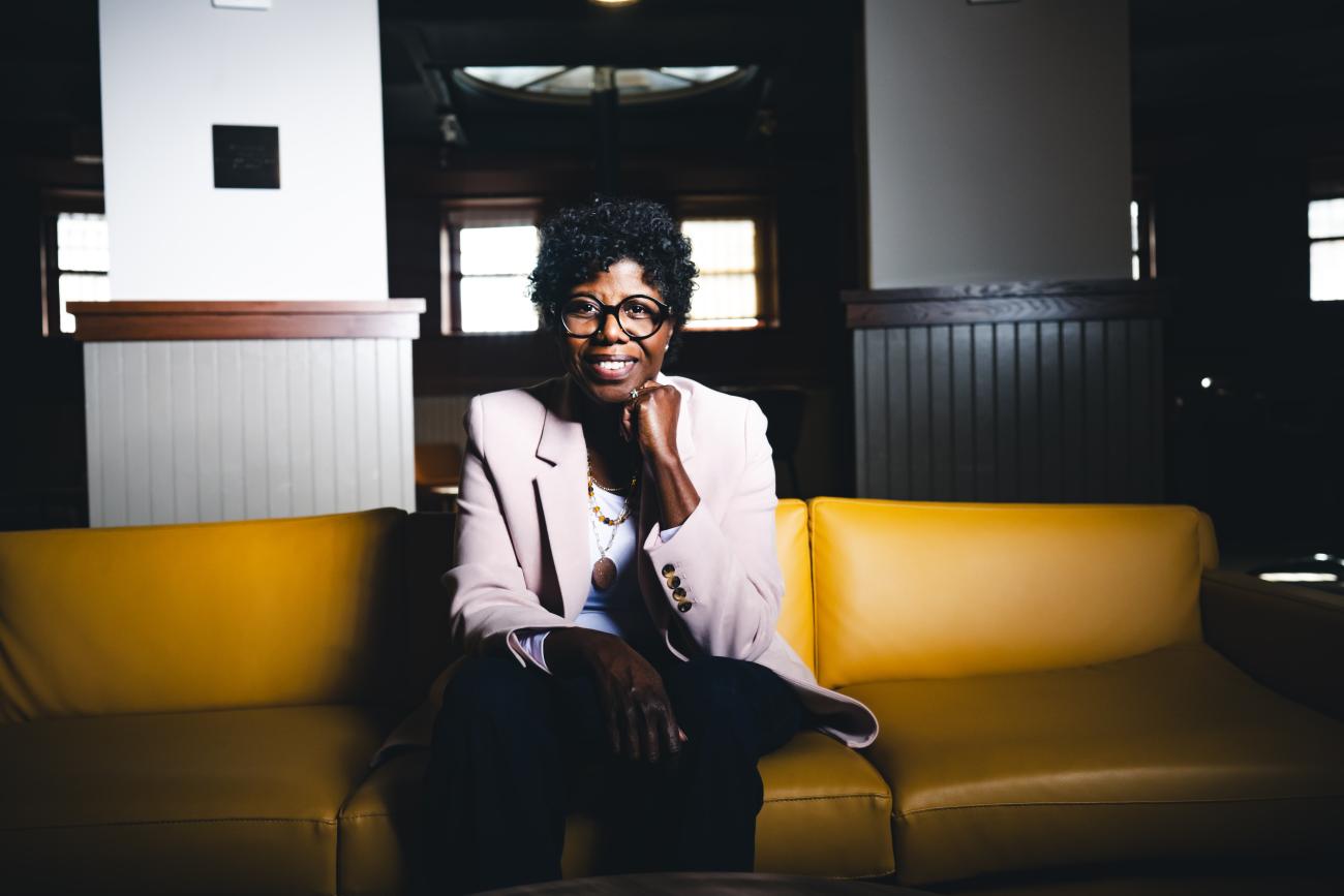 Robin Sundaramoorthy sits on a yellow sofa and smiles at the camera.